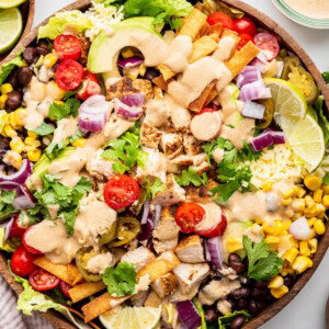 A southwest chicken salad in a large wooden bowl topped with a creamy southwest dressing.